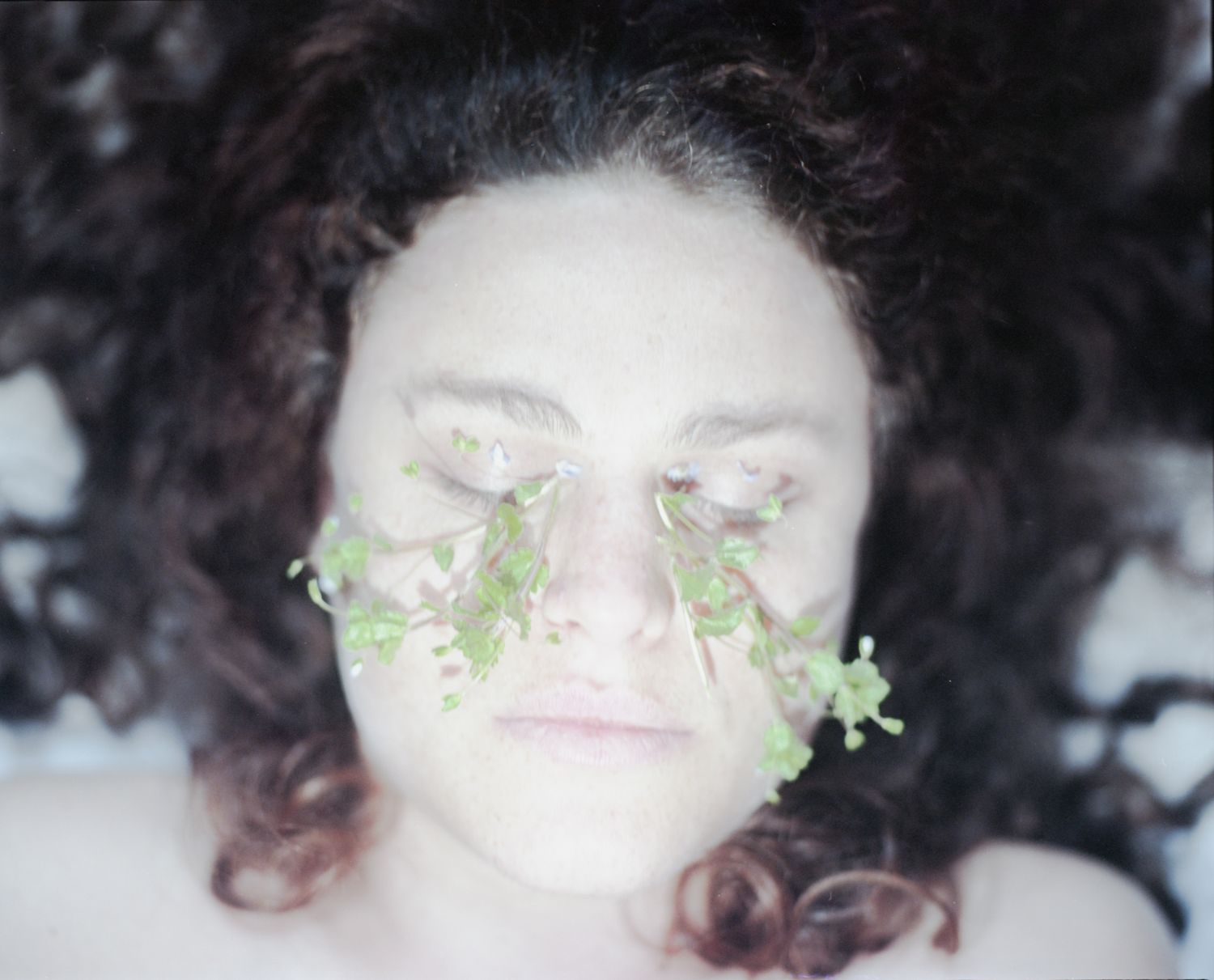 A face with small plants over the closed eyes