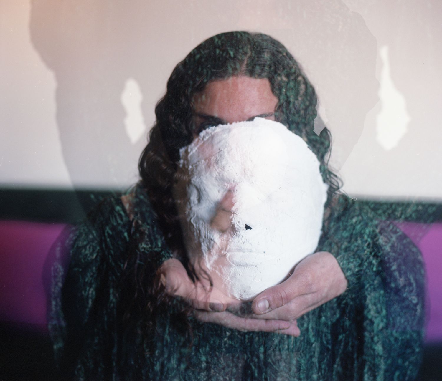 A person holds a white plaster mask in front of their face