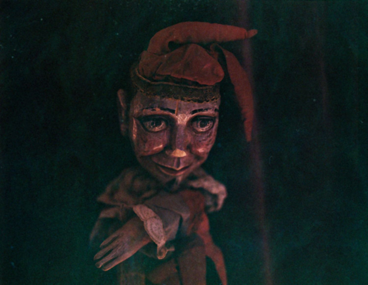 A small carved puppet-like figure in a red hat in the dark