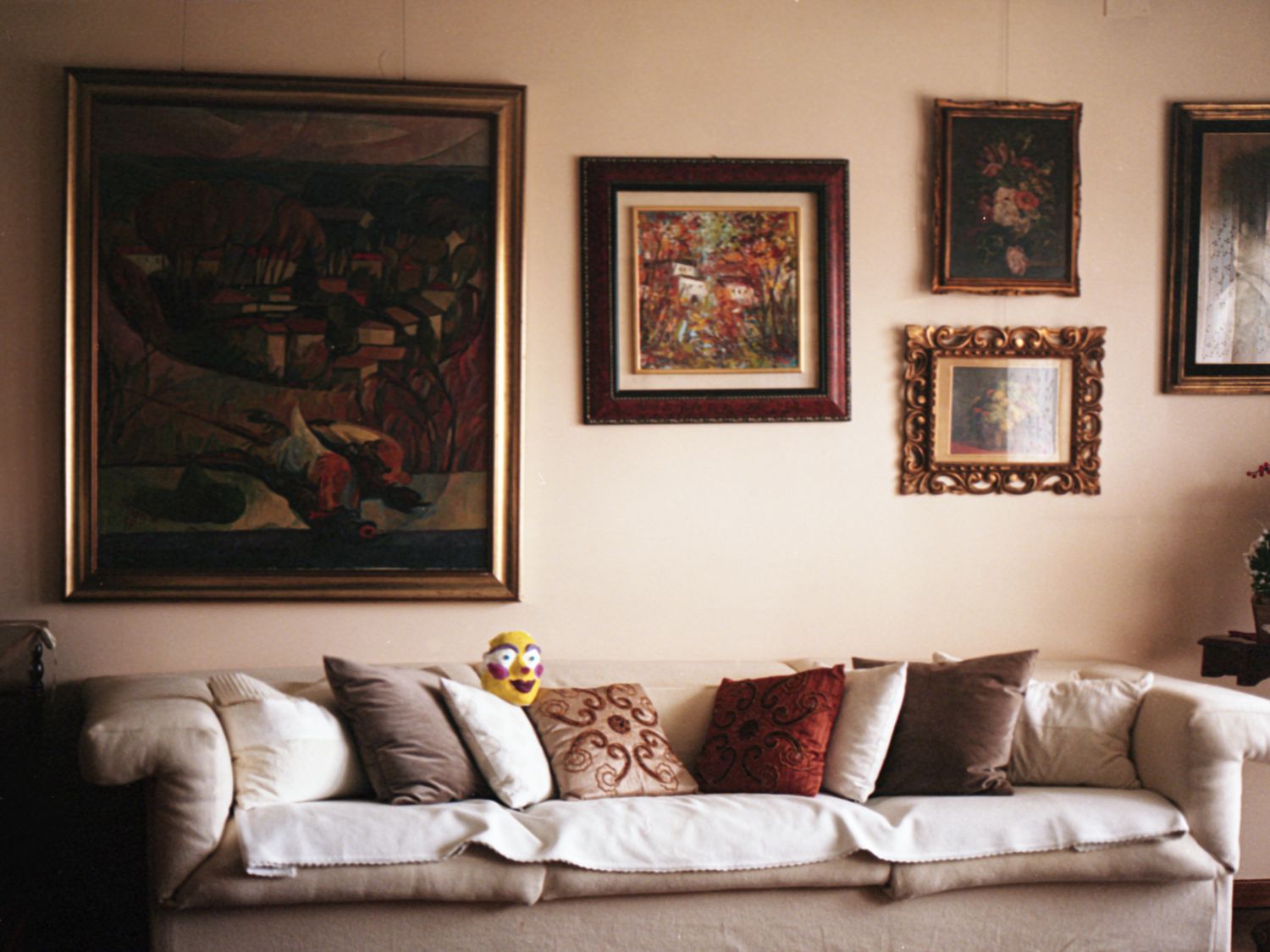 An empty sofa in a room with framed paintings, a small yellow mask resting on it