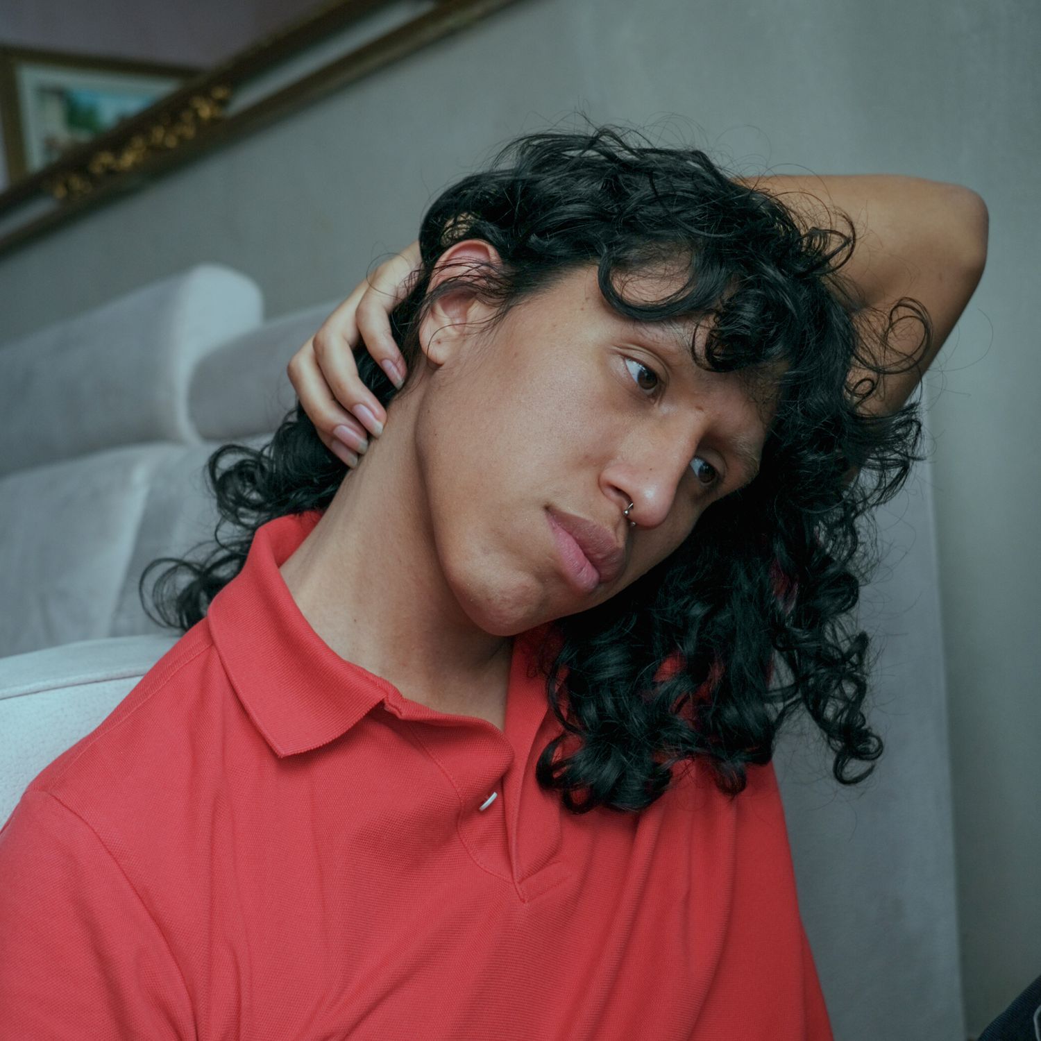 A person with dark curly hair tilts their head, wearing a red polo