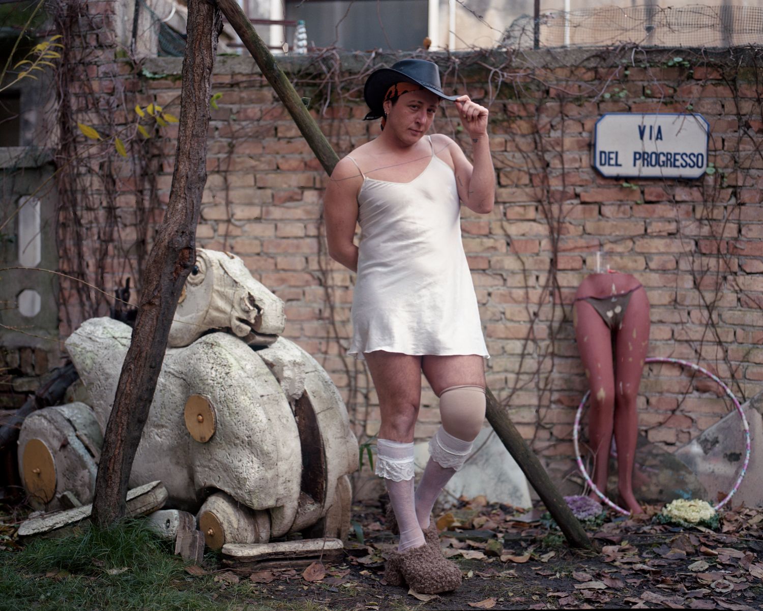 A person in a white slip dress and cowboy hat against a brick wall