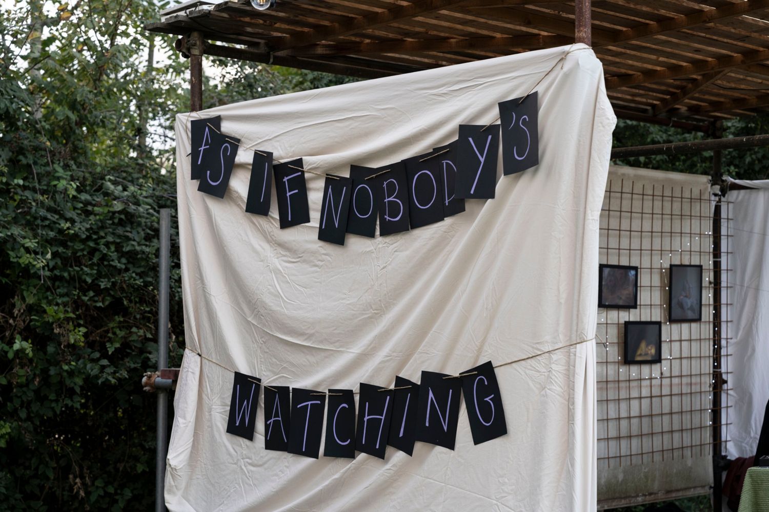 A hand-lettered banner reading As If Nobody’s Watching on a white sheet at the festival